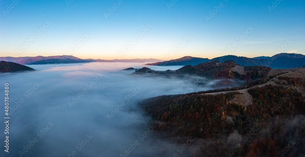 Thick fog among peaks of high autumn mountains at sunrise