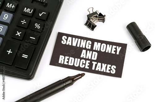 On a white table there is a calculator, a marker and a black plate with the inscription - Saving Money and Reduce Taxes