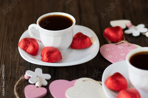 Valentine's Day concept. Two white cups of coffee and heart-shaped sweets on a brown wooden background.