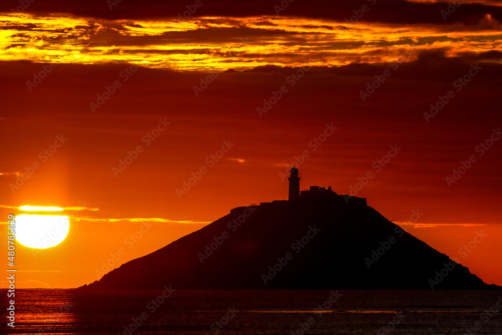 The sunrise at Ballynamona beach in county Cork, Ireland, with Ballycotton Lighthouse in the background