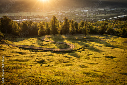 Beautiful curvy country road with fir trees in background during the sunrise with rays of light. Comanesti, Romania photo