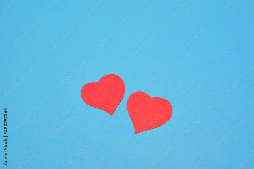 two red paper hearts on blue background, place for text