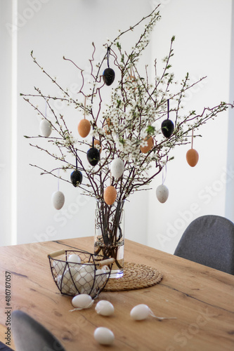 Photography Fresh flowering branches decorated with easter colorful eggs in a vase on a wooden table