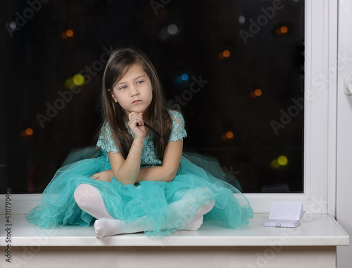 little girl sitting on the windowsill with a pensive expression lisa in her hand she holds a pen