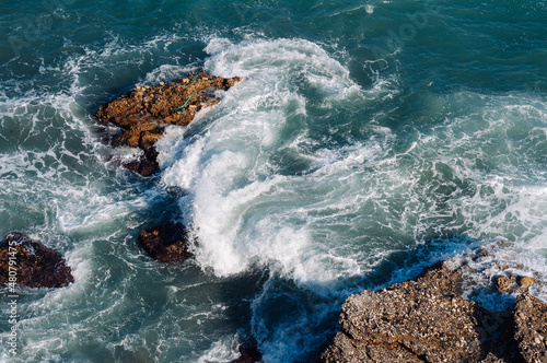 Aerial drone view of the ocean and waves crashing on rocks.