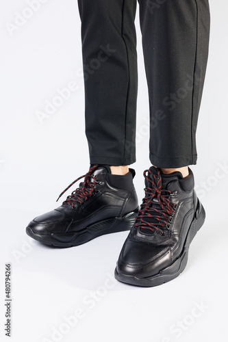 Stylish leather black short men's autumn sneakers on a white background on men's legs. Sneakers winter collection 2022.