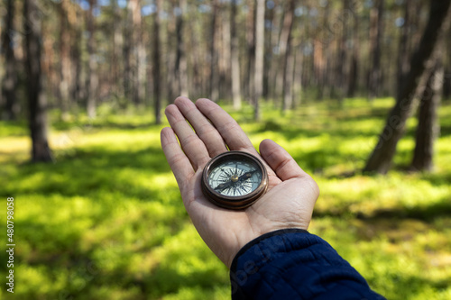 Man holding Cool Antique Vintage Style Travel Compass in hand in middle of beautiful pine tree forest with natural light .