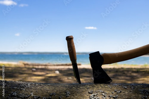 ..Knife and axe on a log in the forest near the lake. Travel,hiking concept. Summer forest. Copy space