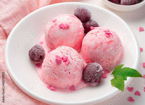 Three balls of ice cream with frozen cherries and hearts in a white plate.