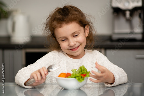 Two cute sisters' girls cut a salad from fresh vegetables. The girls are in the kitchen at home. They socialize and have fun while cooking. The concept of healthy eating. Healthy food. Childhood.