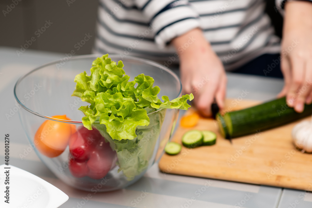 Fresh vegetables in a transparent plate on the table. Healthy eating. Nearby you can see the hands of a man who cuts a salad. The concept of healthy food. Health care. Fresh vegetables in a transparent plate on the table. Healthy eating. Nearby you can see the hands of a man who cuts a salad. The concept of healthy food. Health care.