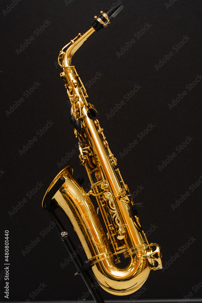 Naklejka premium Saxophone musician instrument on stand on black background. Sax musical instrument for play jazz.
