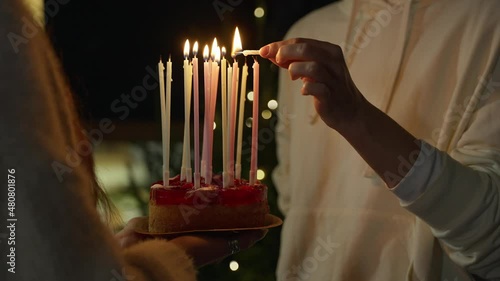 Close-up. Hands light candles on a birthday cake. Tall multicolored candles.
