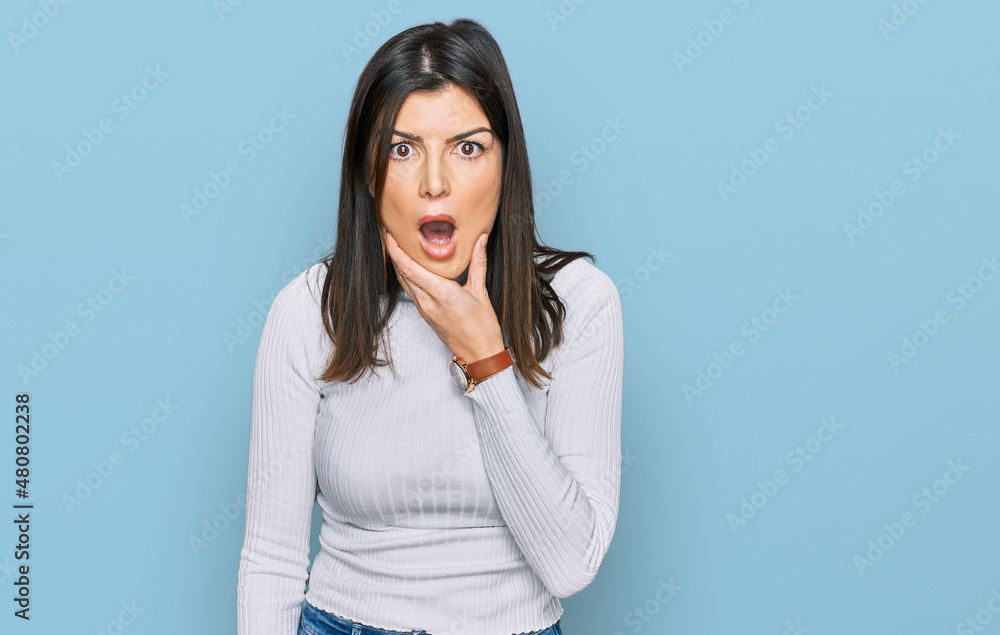 Beautiful brunette woman wearing casual clothes looking fascinated with disbelief, surprise and amazed expression with hands on chin Beautiful brunette woman wearing casual clothes looking fascinated with disbelief, surprise and amazed expression with hands on chin
