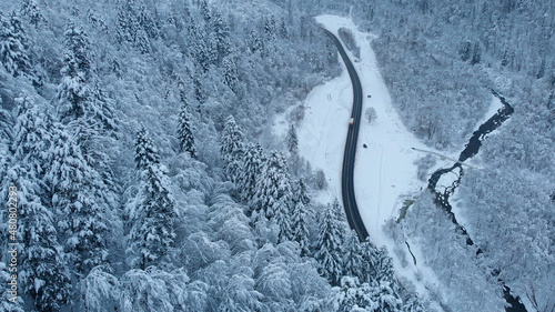 Aerial shot: Trucks driving by the road in winter forest.