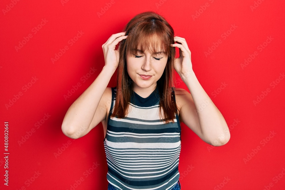 Redhead young woman wearing casual t shirt with hand on head for pain in head because stress. suffering migraine. Redhead young woman wearing casual t shirt with hand on head for pain in head because stress. suffering migraine.