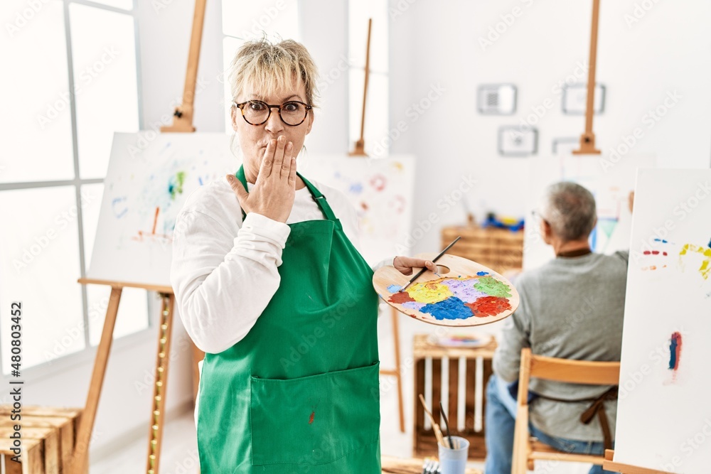 Middle age caucasian woman drawing canvas at art studio covering mouth with hand, shocked and afraid for mistake. surprised expression Middle age caucasian woman drawing canvas at art studio covering mouth with hand, shocked and afraid for mistake. surprised expression