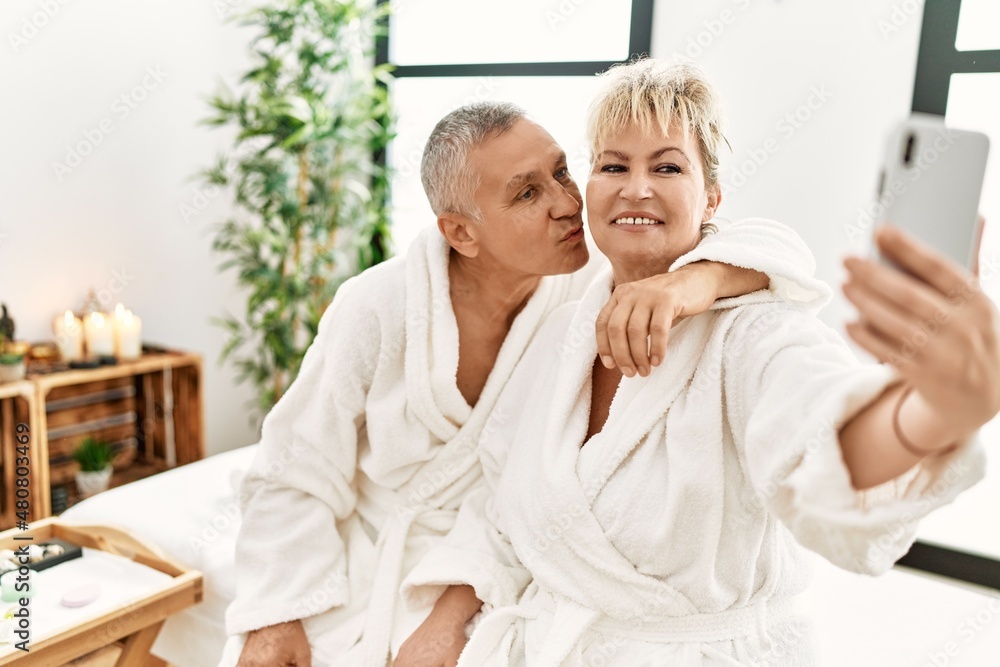 Senior caucasian couple smiling happy making selfie by the smartphone sitting on massage table at beauty center. Senior caucasian couple smiling happy making selfie by the smartphone sitting on massage table at beauty center.