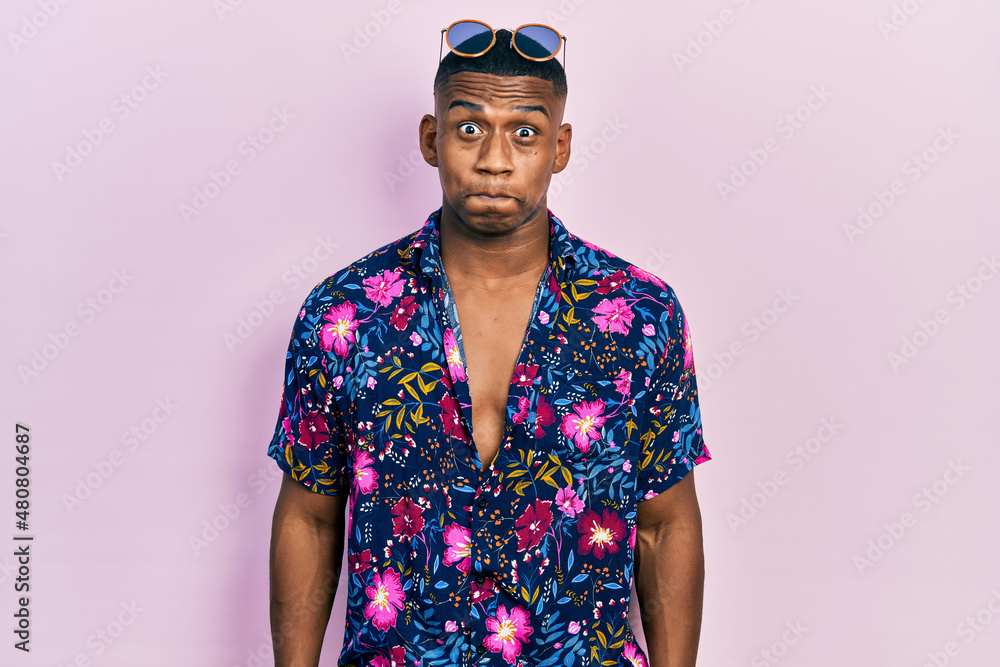 Young black man wearing hawaiian shirt and sunglasses puffing cheeks with funny face. mouth inflated with air, crazy expression. Young black man wearing hawaiian shirt and sunglasses puffing cheeks with funny face. mouth inflated with air, crazy expression.