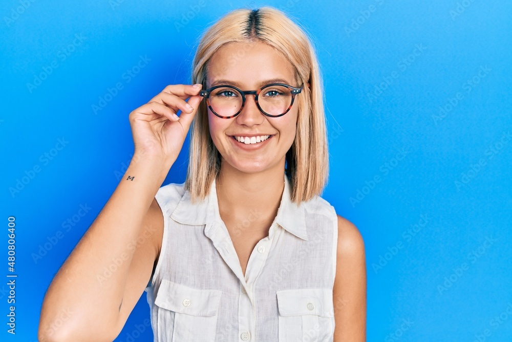 Beautiful blonde woman wearing glasses looking positive and happy standing and smiling with a confident smile showing teeth Beautiful blonde woman wearing glasses looking positive and happy standing and smiling with a confident smile showing teeth