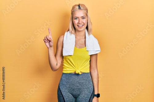 Beautiful blonde sports woman wearing workout outfit pointing finger up with successful idea. exited and happy. number one.