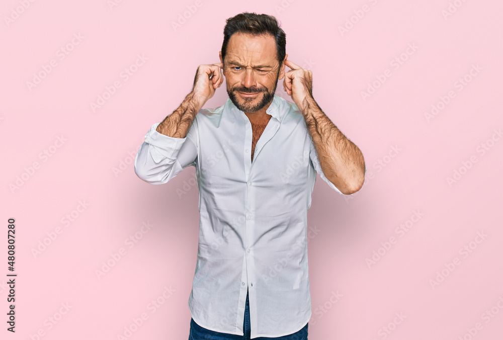 Middle age man wearing casual clothes covering ears with fingers with annoyed expression for the noise of loud music. deaf concept. Middle age man wearing casual clothes covering ears with fingers with annoyed expression for the noise of loud music. deaf concept.