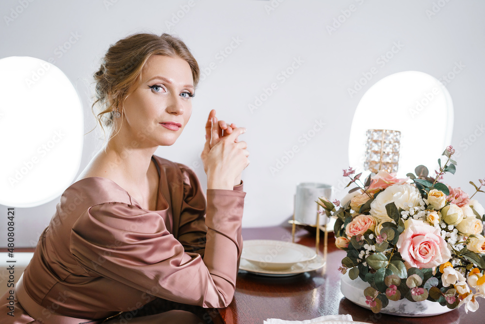 Beautiful young woman inside private jet. Pretty woman sits on passenger seat in beautiful dress with hair and makeup in a comfortable plane by the window. Beautiful young woman inside private jet. Pretty woman sits on passenger seat in beautiful dress with hair and makeup in a comfortable plane by the window.
