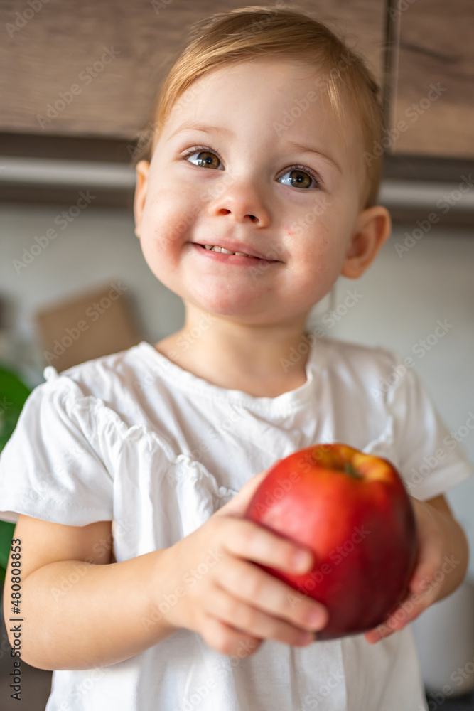 Baby girl blonde eating an apple in the kitchen, concept of healthy food for children Baby girl blonde eating an apple in the kitchen, concept of healthy food for children