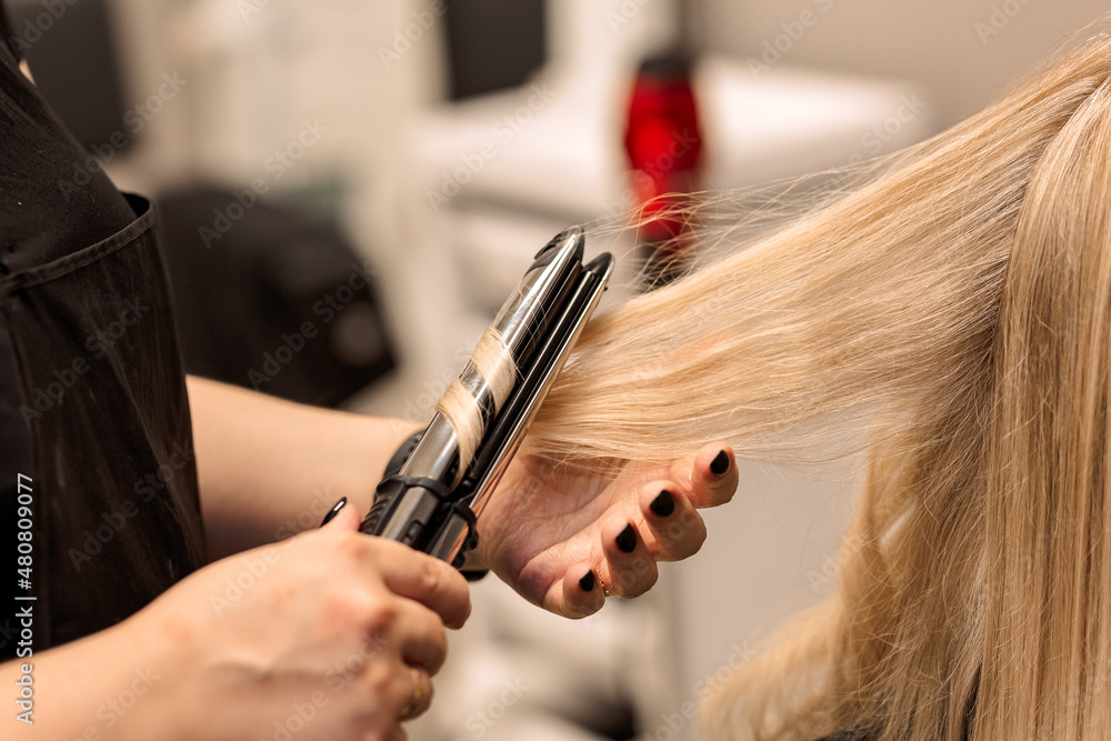 Naklejka premium The hairdresser curls the hair of the client with a hair straightener