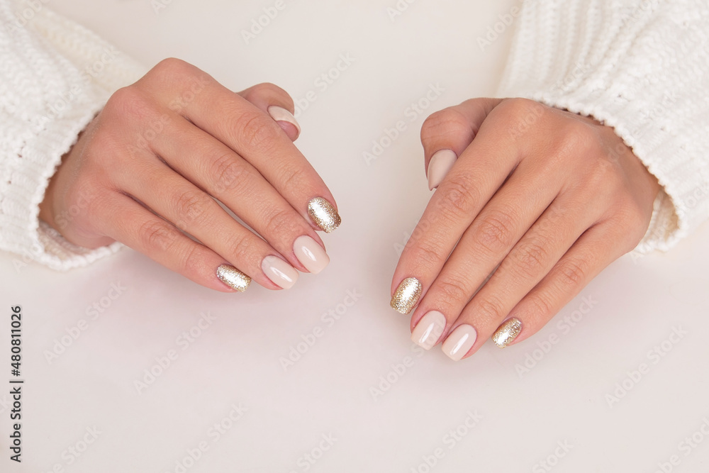 Beautiful female hands with beige and golden manicure nails on white background