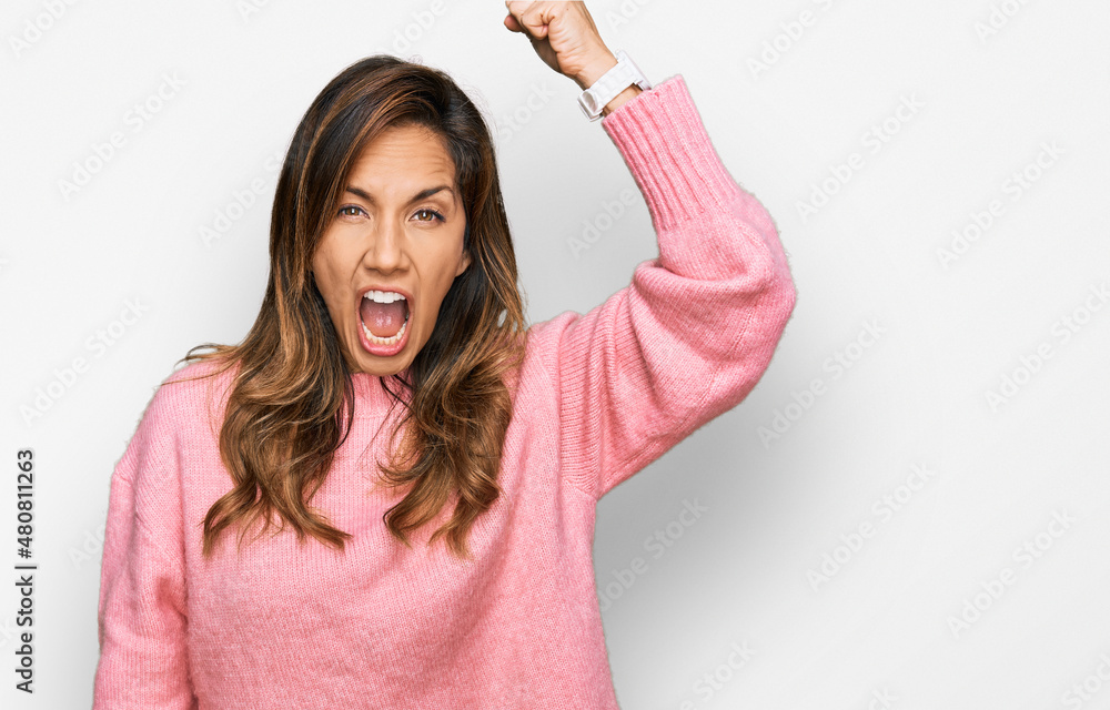 Young hispanic woman wearing casual clothes angry and mad raising fist frustrated and furious while shouting with anger. rage and aggressive concept. Young hispanic woman wearing casual clothes angry and mad raising fist frustrated and furious while shouting with anger. rage and aggressive concept.