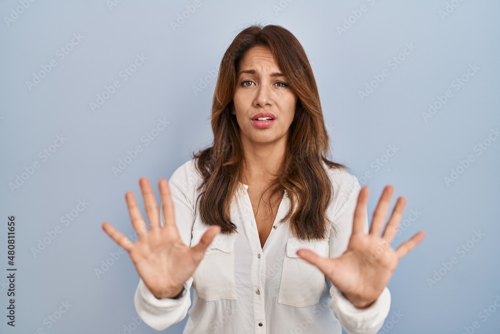 Hispanic woman standing over isolated background moving away hands palms showing refusal and denial with afraid and disgusting expression. stop and forbidden. Hispanic woman standing over isolated background moving away hands palms showing refusal and denial with afraid and disgusting expression. stop and forbidden.