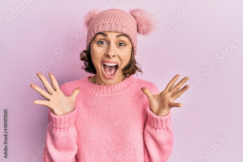 Young brunette woman wearing cute wool cap celebrating crazy and amazed for success with arms raised and open eyes screaming excited. winner concept