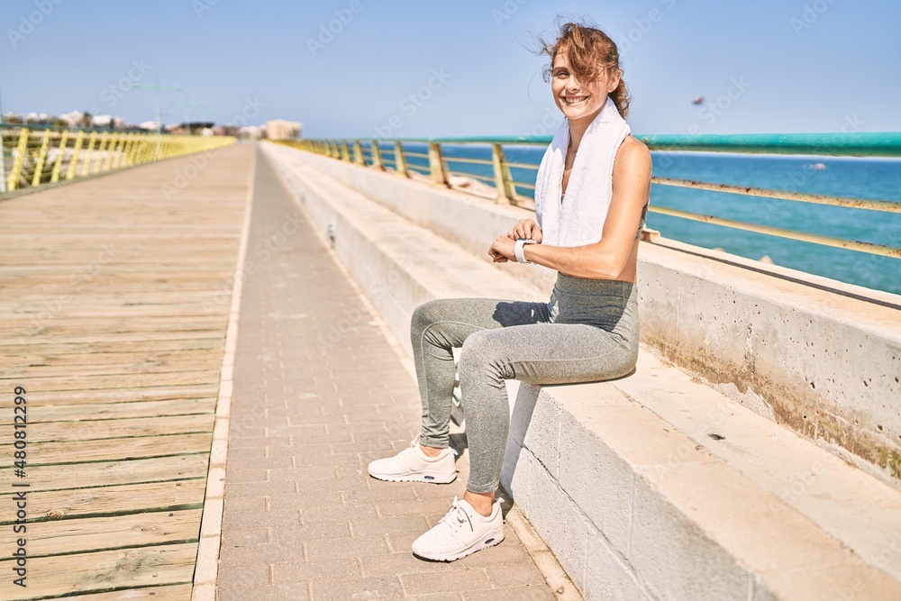 Young caucasian woman wearing sportswear looking watch at seaside