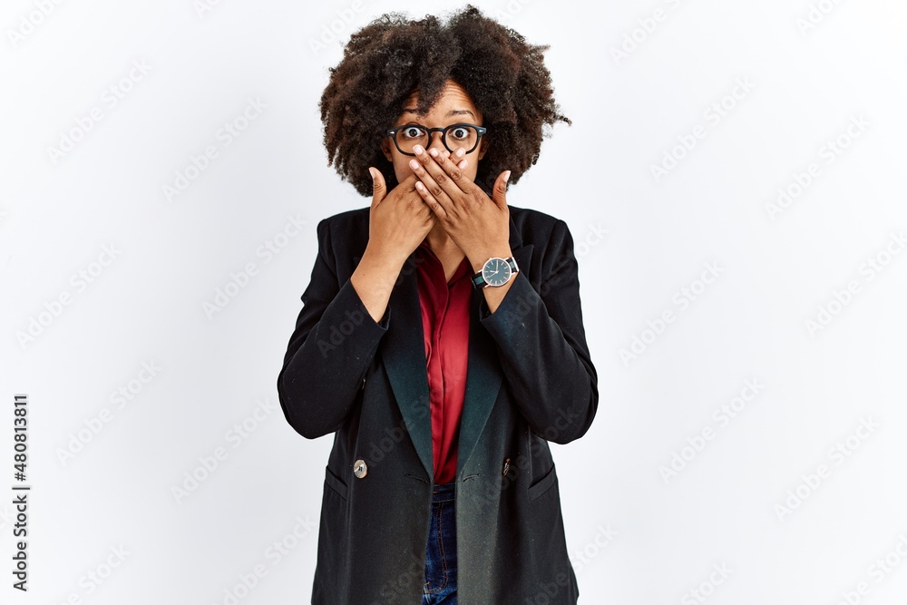 African american woman with afro hair wearing business jacket and glasses shocked covering mouth with hands for mistake. secret concept. African american woman with afro hair wearing business jacket and glasses shocked covering mouth with hands for mistake. secret concept.