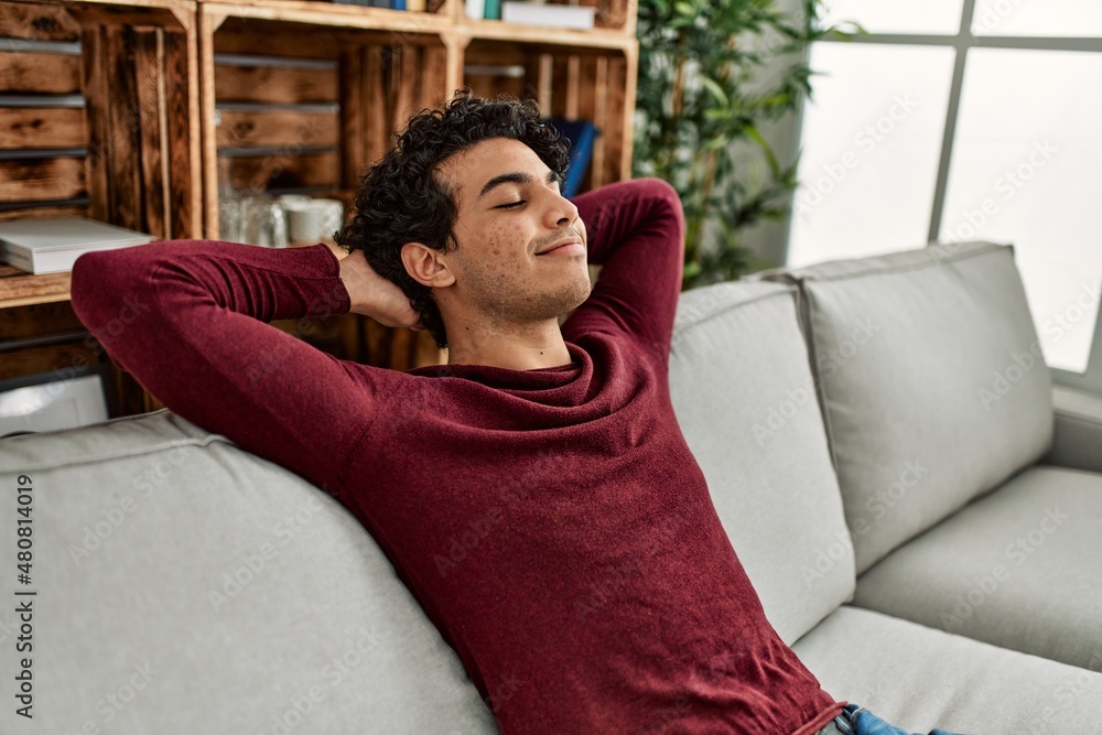 Young hispanic man relaxing with hands on head sitting on the sofa at home. Young hispanic man relaxing with hands on head sitting on the sofa at home.