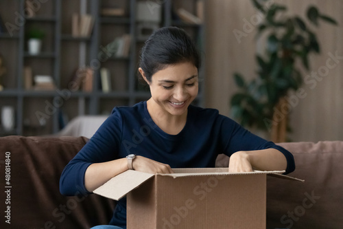 Curious smiling millennial beautiful Indian ethnicity woman unpacking parcel in cardboard box, feeling excited of getting wished item from favorite internet store, satisfied with online shopping. © fizkes
