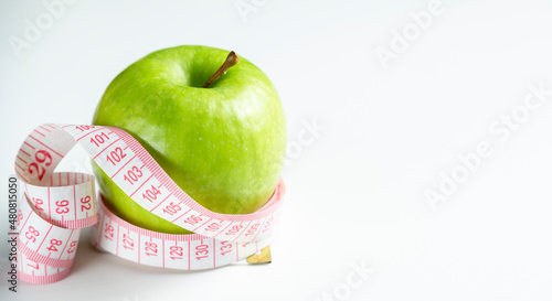 a whole green apple on a white background with a meter (measuring tape)