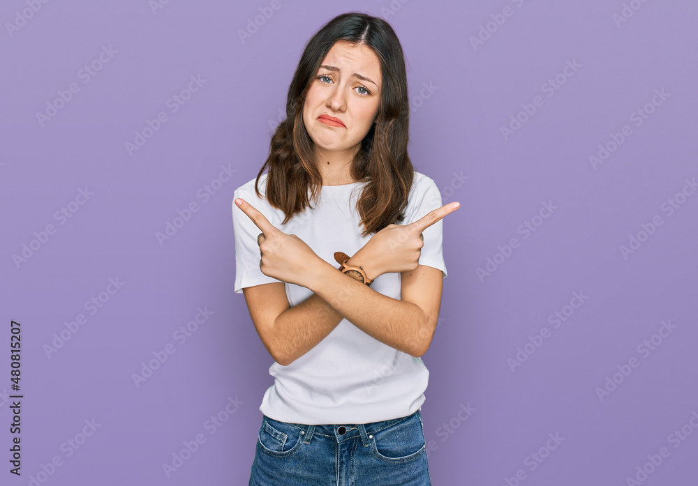Young beautiful woman wearing casual white t shirt pointing to both sides with fingers, different direction disagree Young beautiful woman wearing casual white t shirt pointing to both sides with fingers, different direction disagree