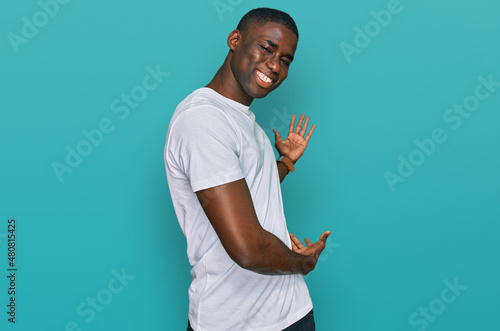 Young african american man wearing casual white t shirt inviting to enter smiling natural with open hand