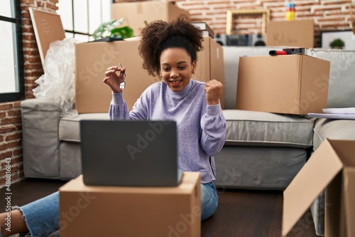 Young african american woman showing keys of new home on video call screaming proud, celebrating victory and success very excited with raised arm