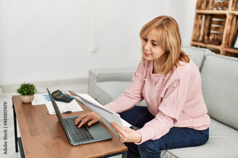 Middle age blonde woman concentrated teleworking sitting on the sofa at home. Middle age blonde woman concentrated teleworking sitting on the sofa at home.