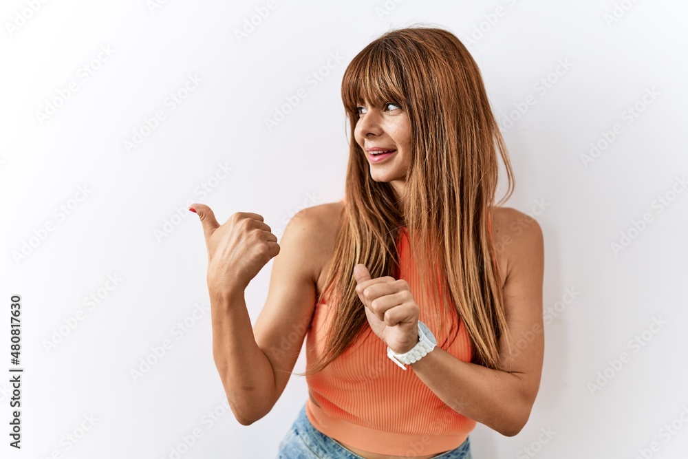 Hispanic woman with bang hairstyle standing over isolated background pointing to the back behind with hand and thumbs up, smiling confident Hispanic woman with bang hairstyle standing over isolated background pointing to the back behind with hand and thumbs up, smiling confident