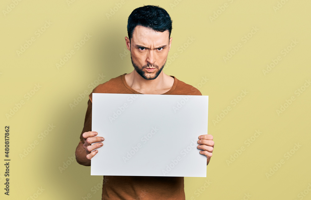 Hispanic man with beard holding blank empty banner skeptic and nervous, frowning upset because of problem. negative person. Hispanic man with beard holding blank empty banner skeptic and nervous, frowning upset because of problem. negative person.