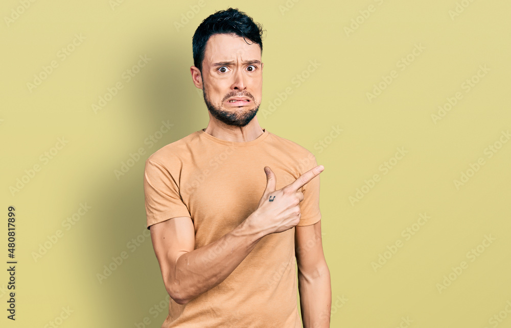 Hispanic man with beard wearing casual t shirt pointing aside worried and nervous with forefinger, concerned and surprised expression Hispanic man with beard wearing casual t shirt pointing aside worried and nervous with forefinger, concerned and surprised expression