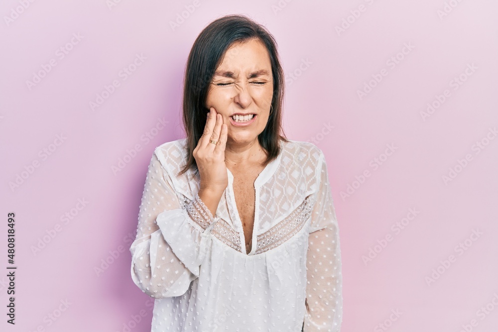 Middle age hispanic woman wearing casual clothes touching mouth with hand with painful expression because of toothache or dental illness on teeth. dentist Middle age hispanic woman wearing casual clothes touching mouth with hand with painful expression because of toothache or dental illness on teeth. dentist