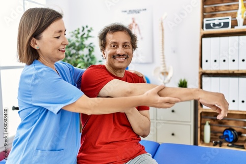 Middle age man and woman wearing physiotherapy uniform having rehab session stretching arm at physiotherapy clinic