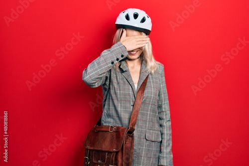 Beautiful caucasian blonde business woman wearing bike helmet smiling and laughing with hand on face covering eyes for surprise. blind concept.