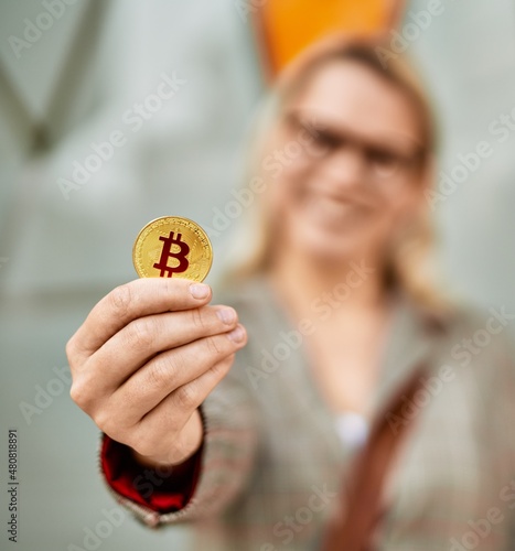Young blonde businesswoman smiling happy holding bitcoin at the city.