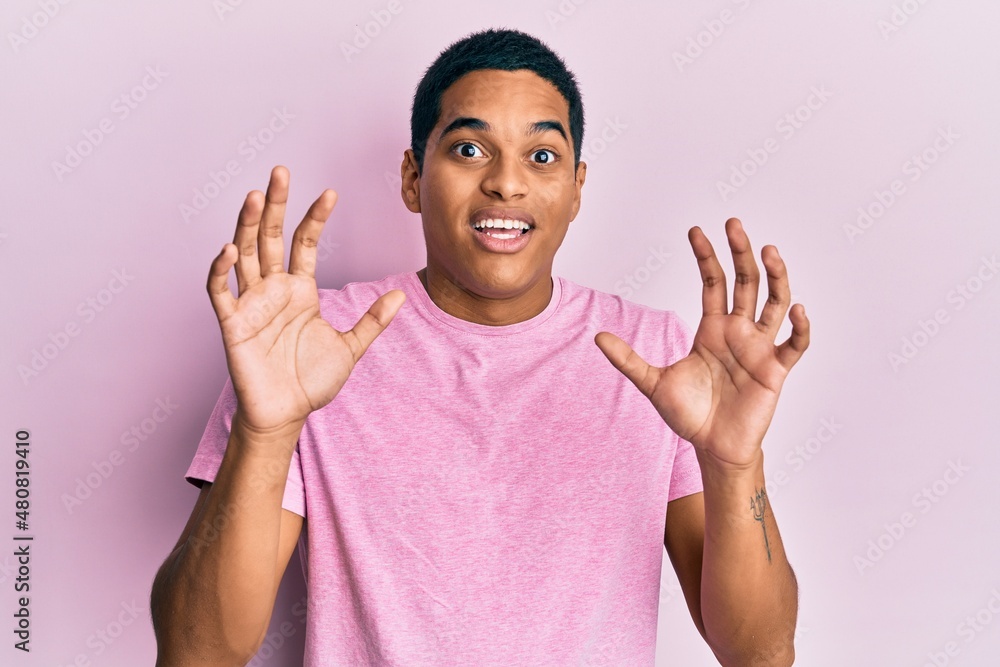 Young handsome hispanic man wearing casual pink t shirt afraid and terrified with fear expression stop gesture with hands, shouting in shock. panic concept.